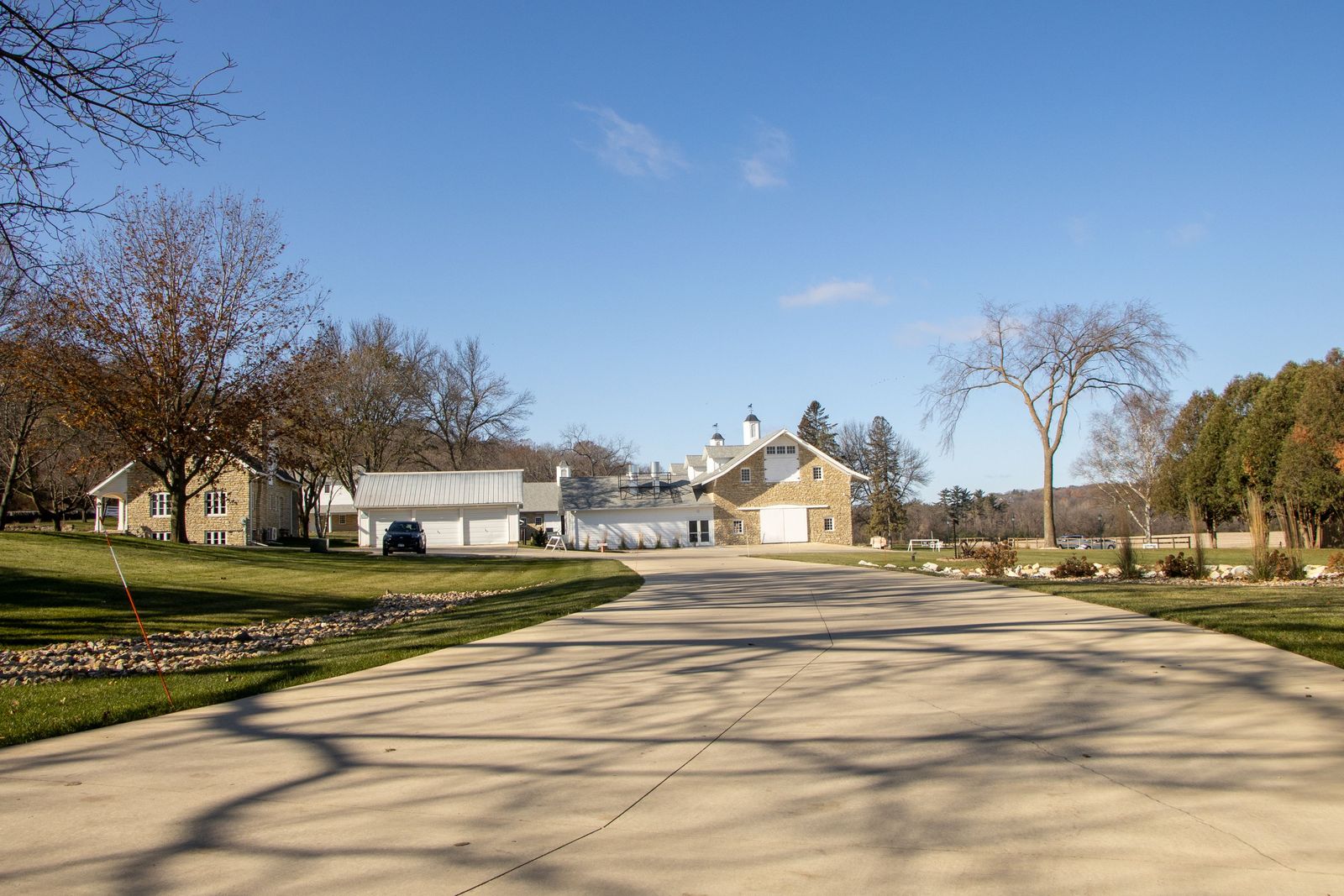 Long concrete driveway running up to a limestone house and outbuildings on acreage