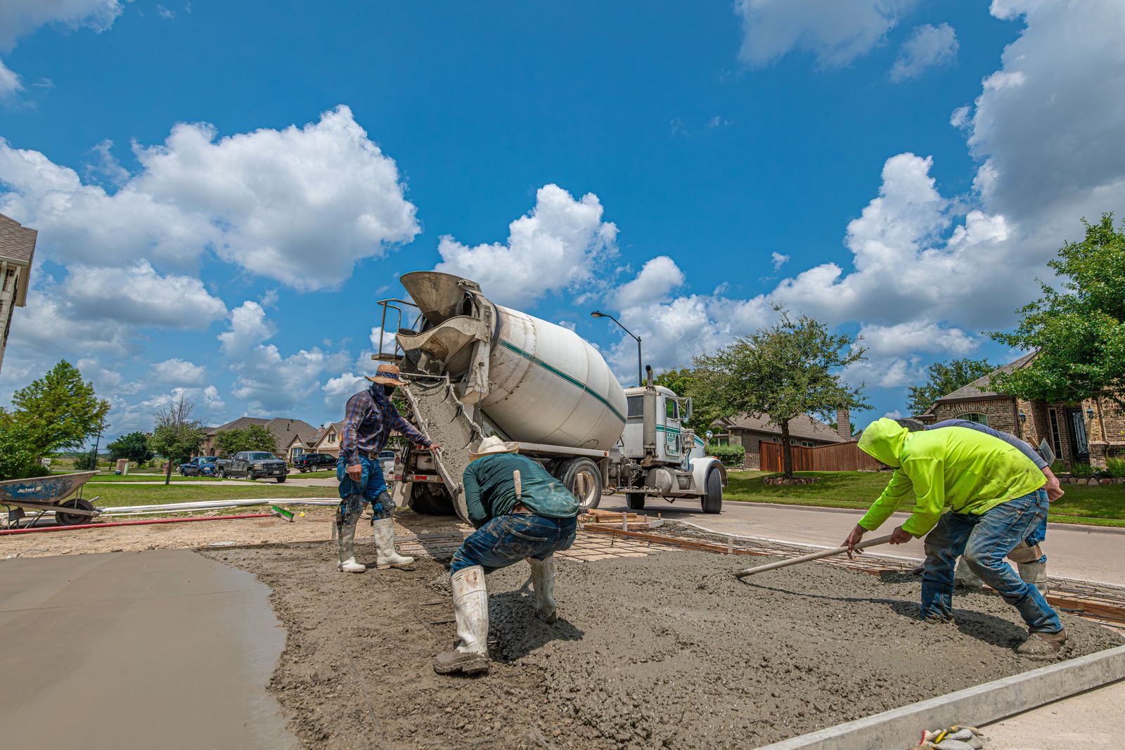 Concrete crew placing and raking a residential driveway pour from a mixer truck in Texas