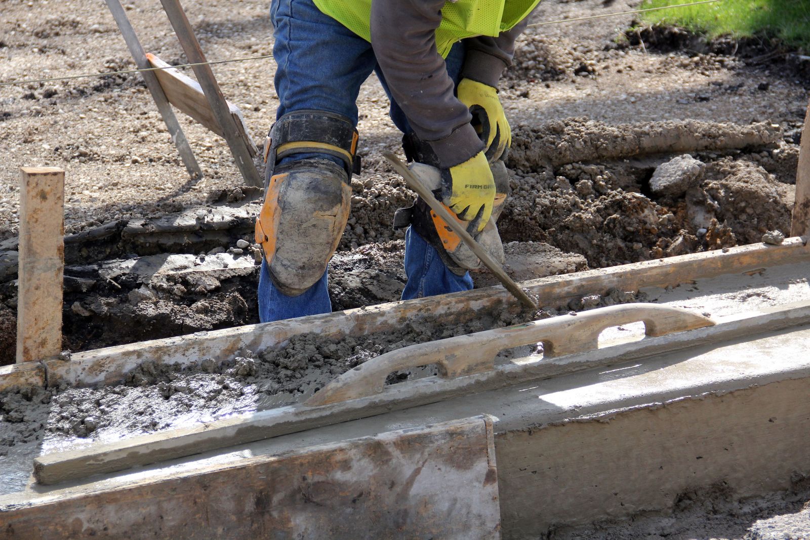 Concrete finisher running an edger along the formed edge of a fresh sidewalk pour