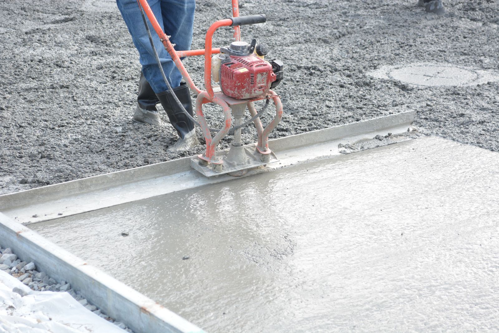 Power screed leveling wet concrete across a formed slab